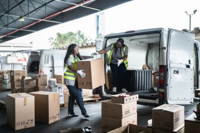 Two female warehouse workers loading van with boxes